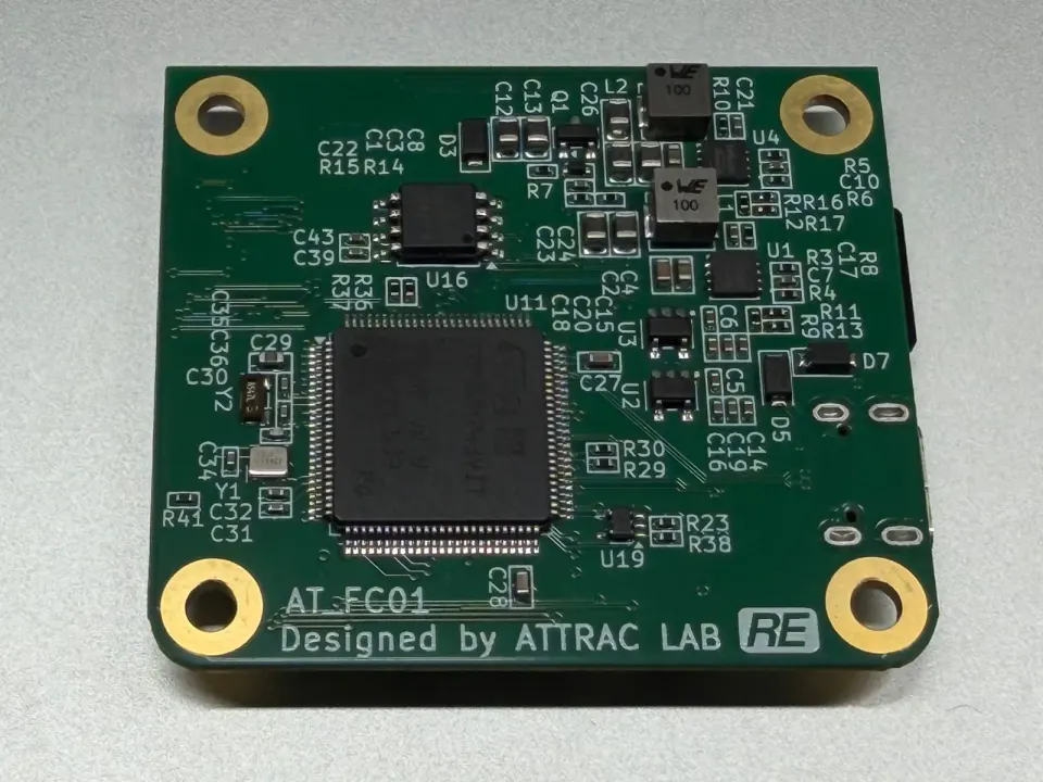 手のひらほどの大きさの緑色の基板。中央に黒いチップがあり、端に「AT_FC01 Designed by ATTRAC LAB」の文字が見える