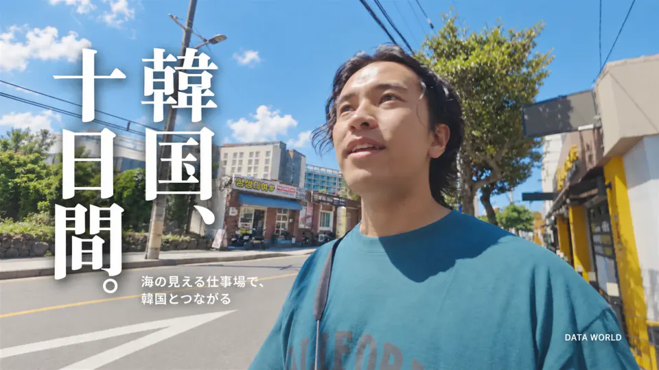 済州島の通りで空を見上げるDATA WORLD編集長の小笠原海人。左に縦書きの「韓国、十日間。」と「海の見える仕事場で、韓国とつながる」の文字